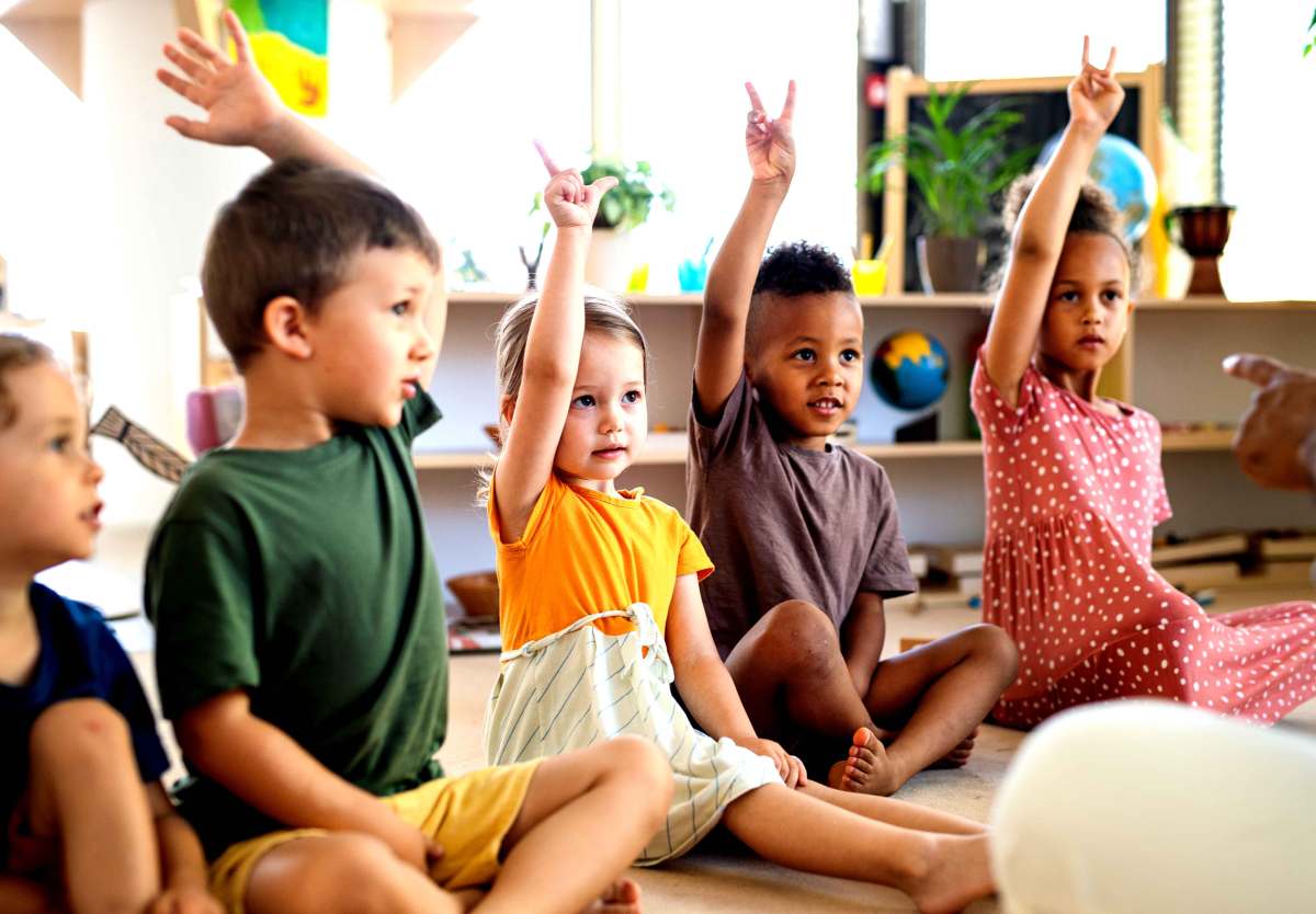 Gruppe von Kindergartenkindern sitzt im Halbkreis, teilweise melden sich die Kinder.