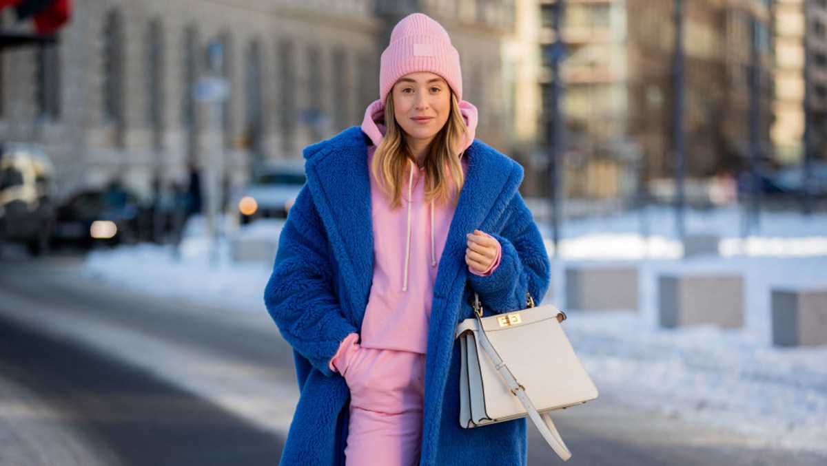 Frau trägt ein Winter-Outfit mit Mütze, Mantel und Swetpants.