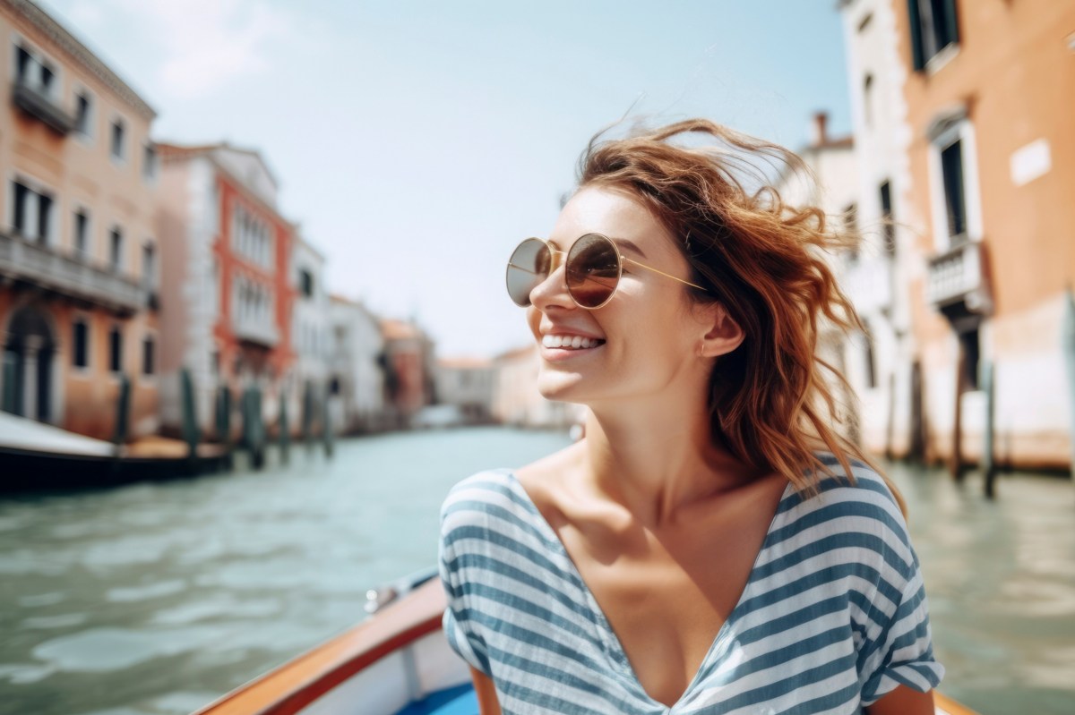 Frau mit Sonnenbrille und einem Streifen-Oberteil sitzt in einer Gracht in Venedig.