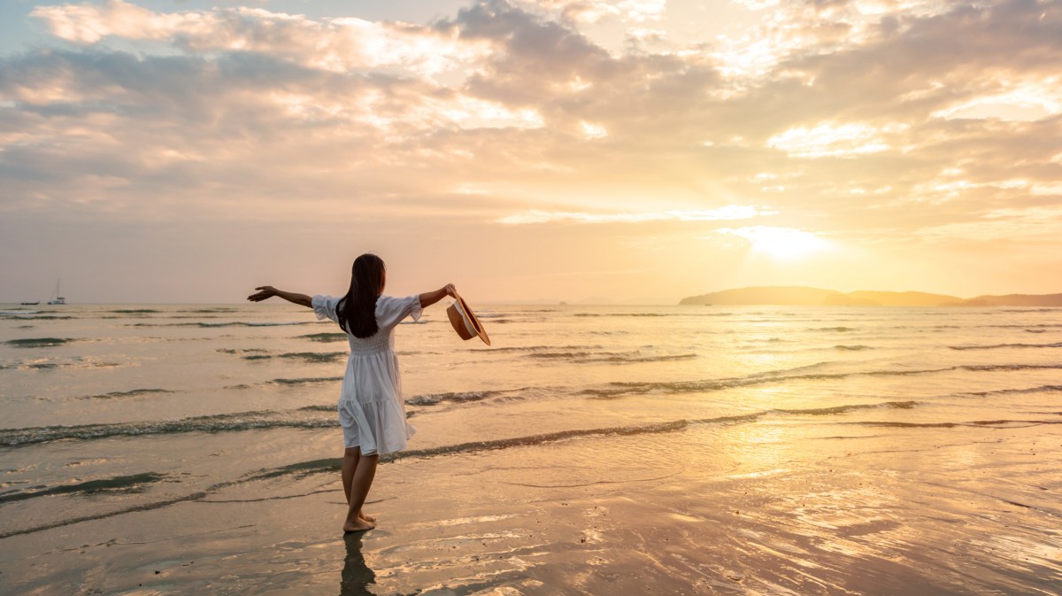 Frau im Sommerkleid am Strand bei Sonnenuntergang