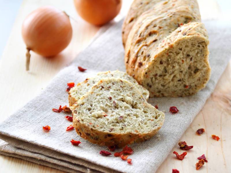 Ein Brot auf einem hellen Tuch, dahinter Zwiebeln.