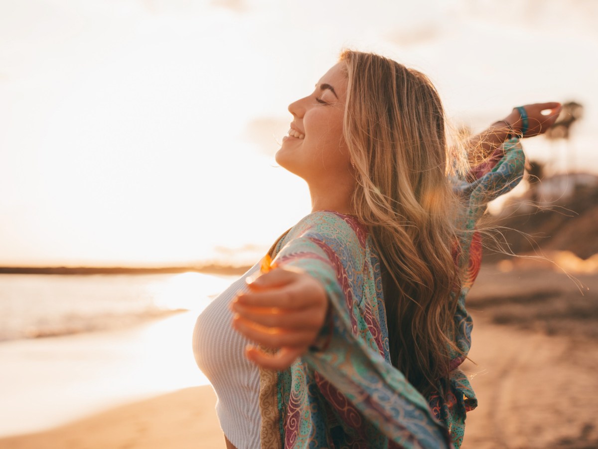 Frau am Strand lächelt und wird von Sonne angestrahlt