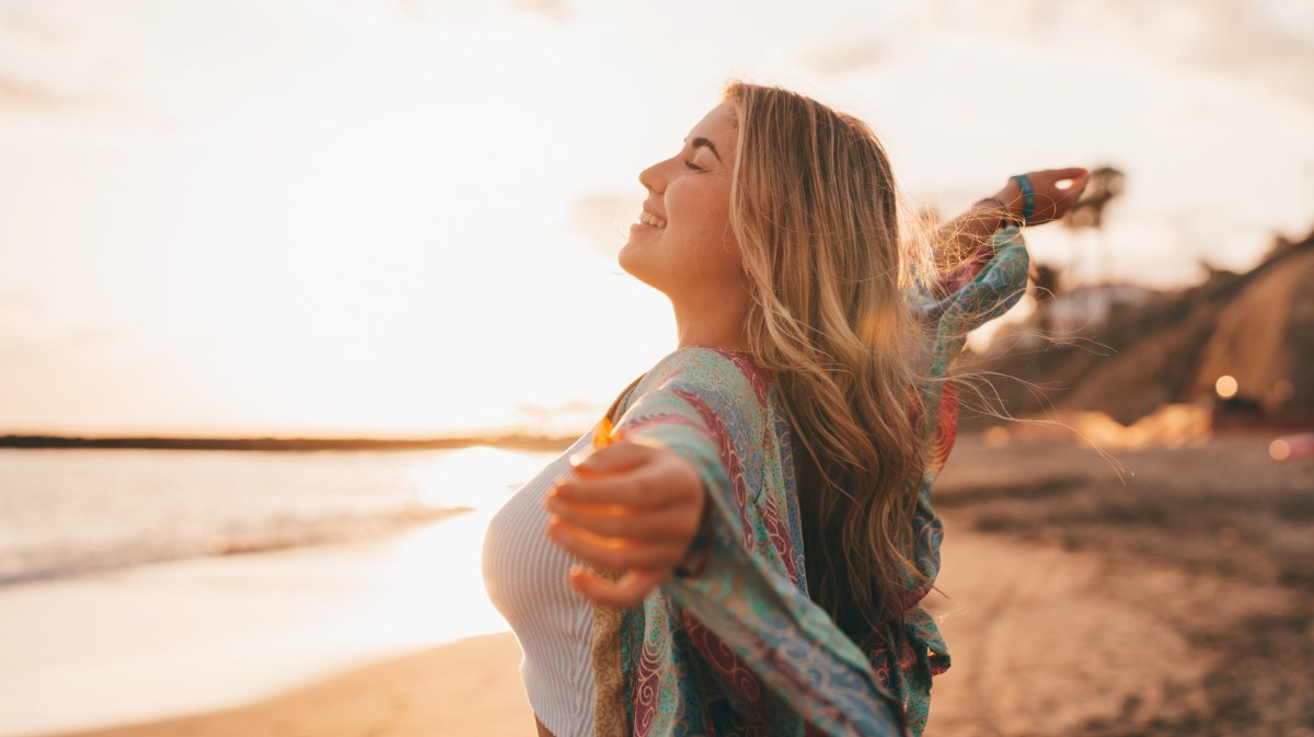 Frau am Strand lächelt und wird von Sonne angestrahlt