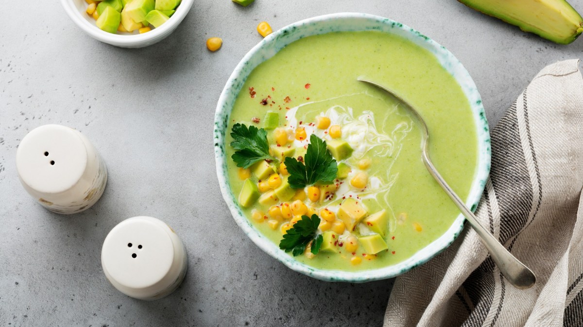 Eine weiße Schale mit der hellgrünen Suppe auf einem grauen Tisch. Alles direkt von oben fotografiert.