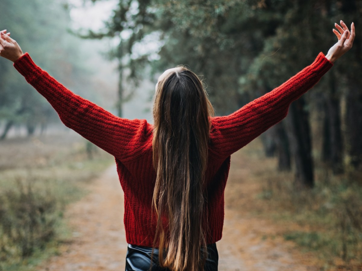 Frau steht im Wald und breitet Arme aus.