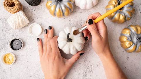 Weibliche Hände mit schwarzen Nägeln malen Kürbisse für Halloween