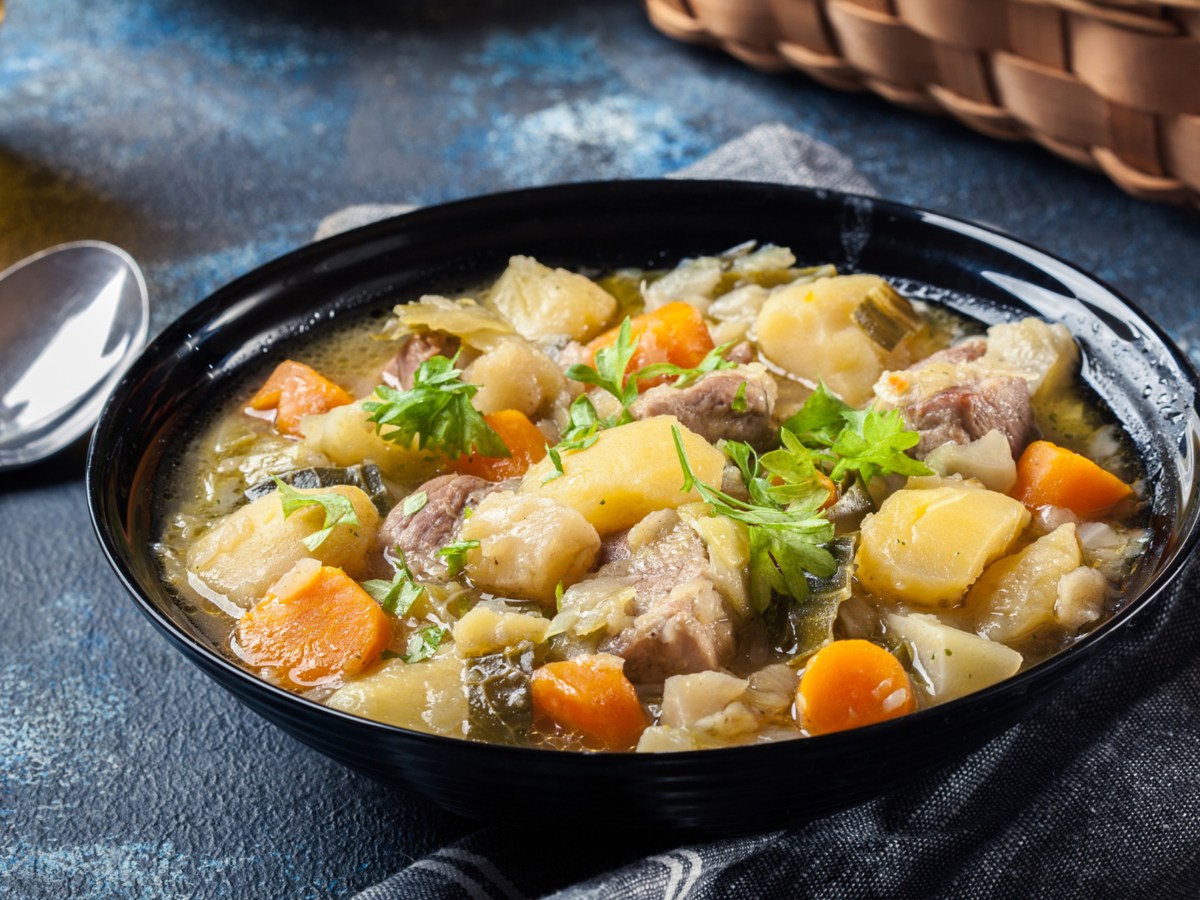 Schwarze Schale mit Pichelsteiner Eintopf, ein Löffel liegt daneben.