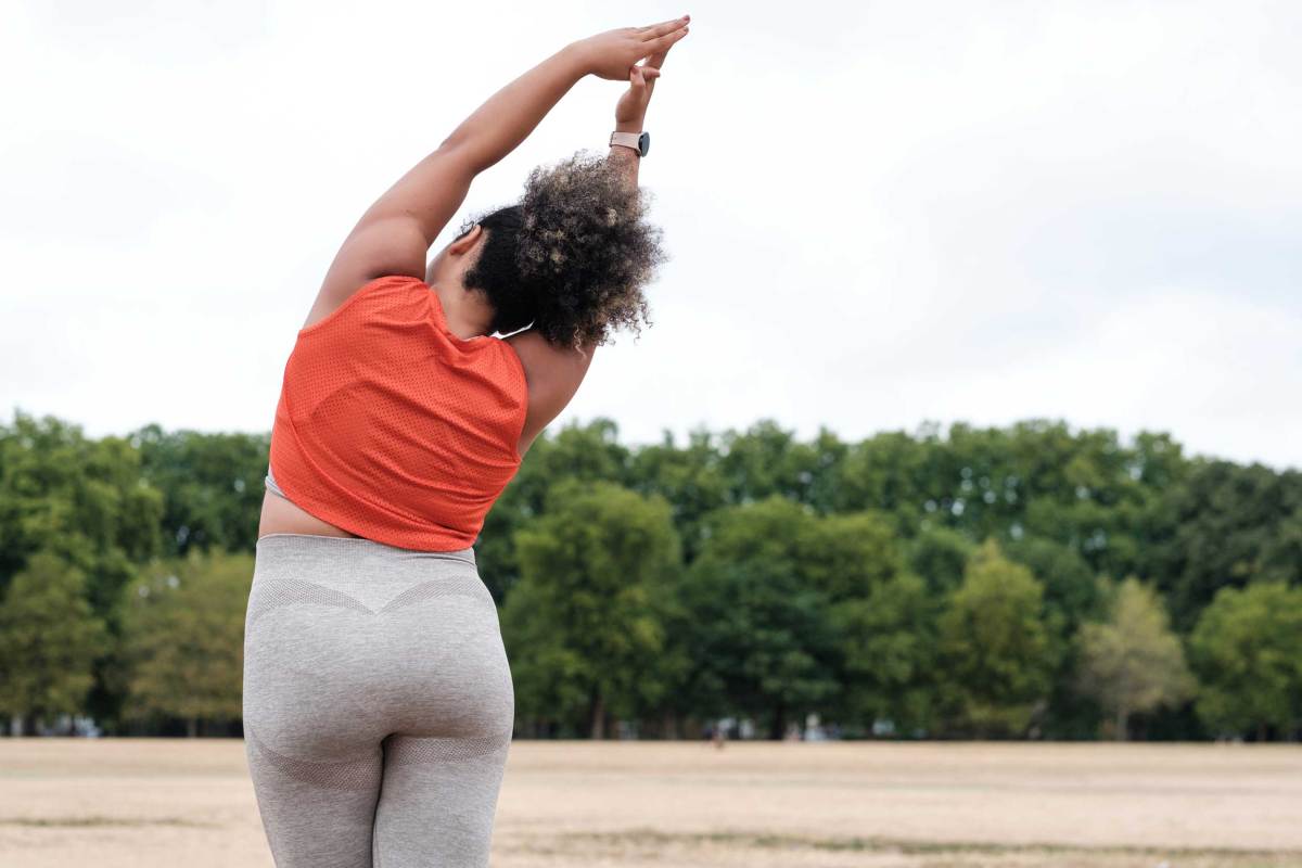 Rückenansicht einer kurvigen Frau, die sich in einem Park in London streckt.