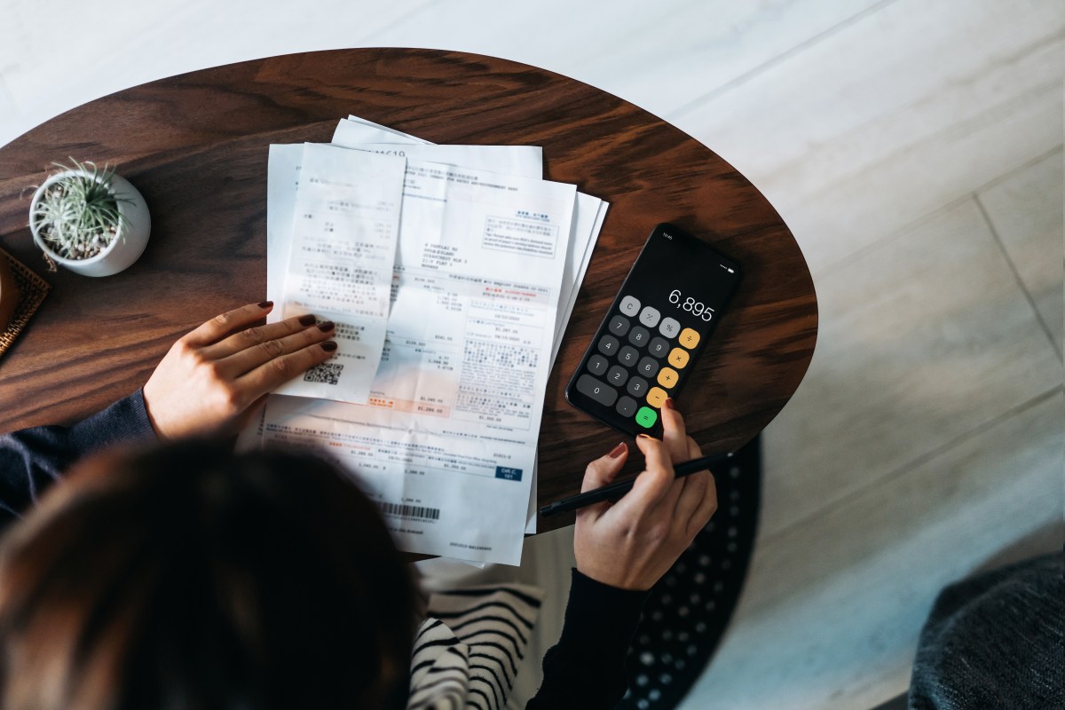 Blick von oben auf eine junge asiatische Frau, die zu Hause persönliche Bank- und Finanzgeschäfte verwaltet. Budget planen und Ausgaben berechnen, während sie ihre Rechnungen mit dem Taschenrechner überprüft. Verwaltung von Steuern und Finanzrechnungen. Hausbudgetierung. Konzept von Finanzen und Wirtschaft