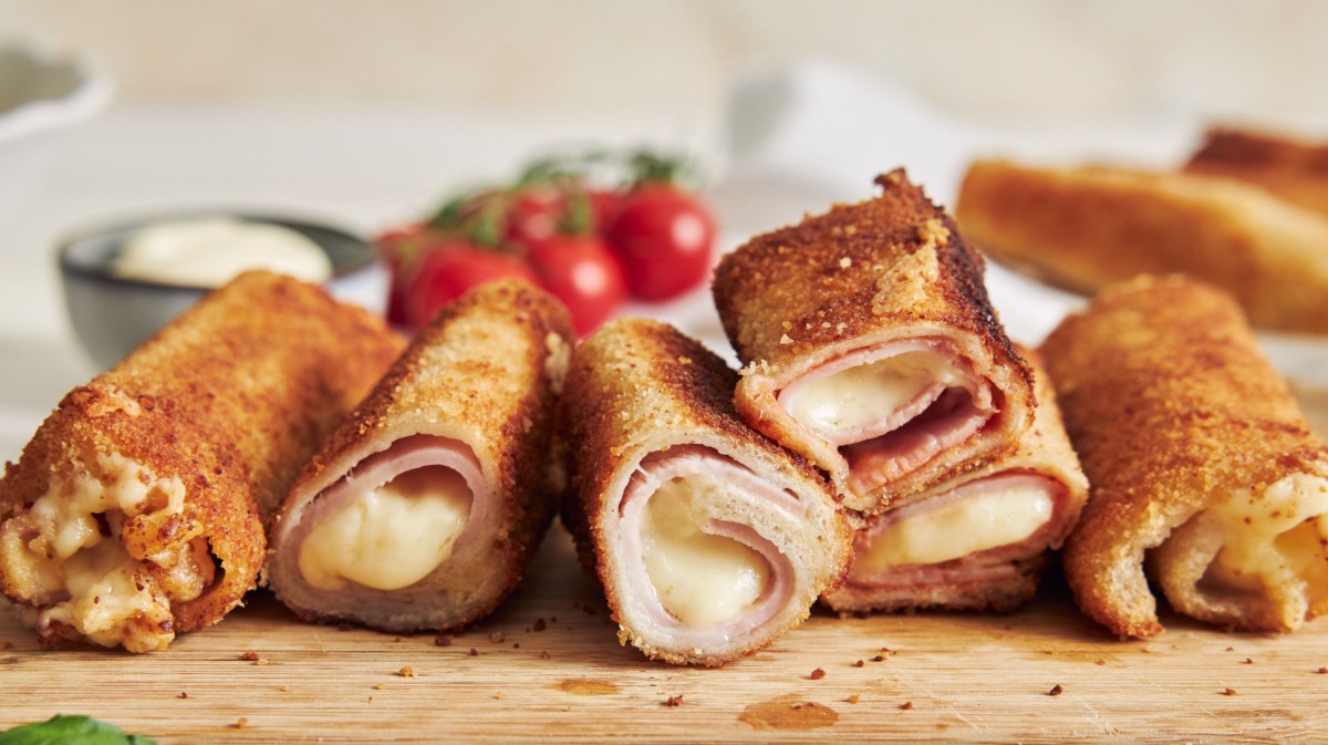 Toaströllchen mit Schinken und Käse auf Holzbrett.