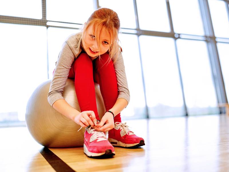 Mädchen sitzt auf einem Gymnastikball und bindet sich die Schuhe.