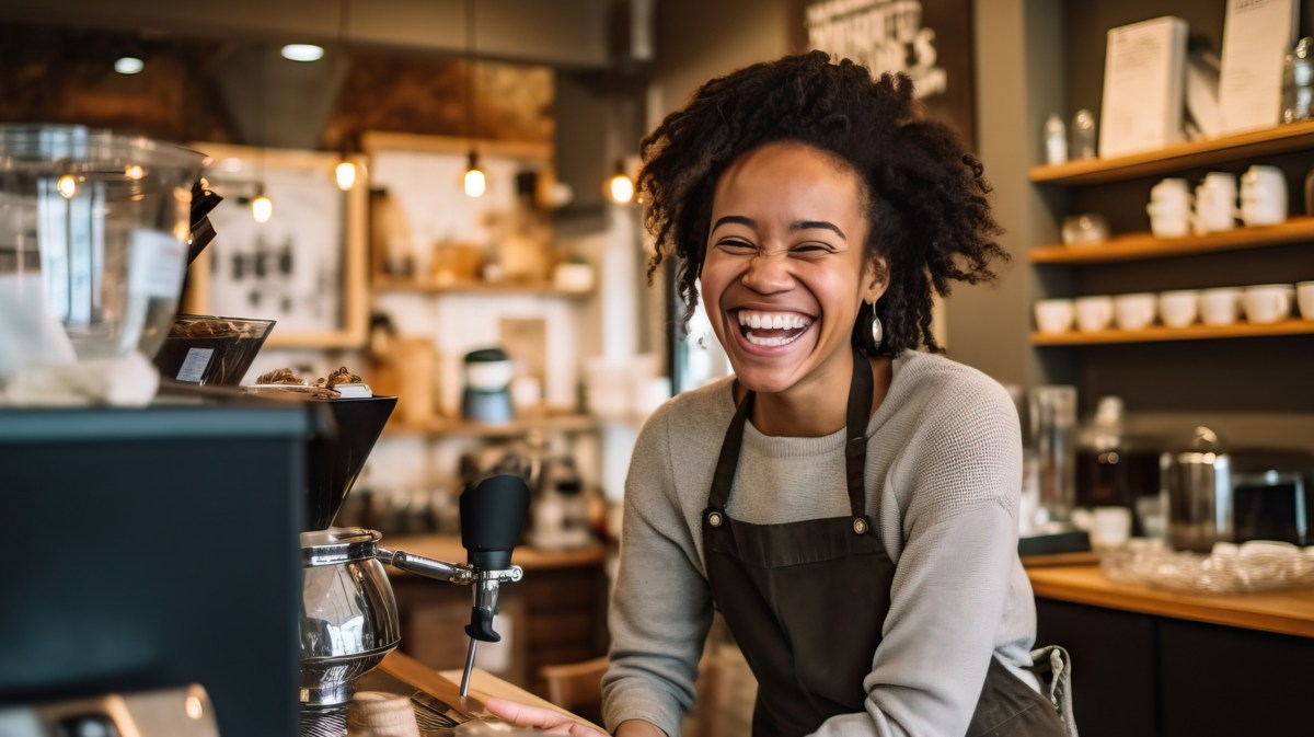 Junge Frau arbeitet als Barista und lacht fröhlich.