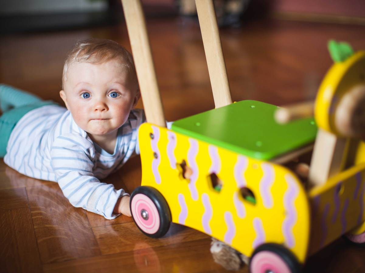 Baby liegt neben einem Lauflernwagen.