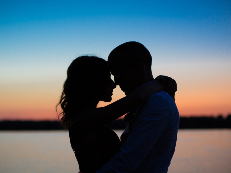 Paar steht Arm in Arm vor einem Sonnenuntergang