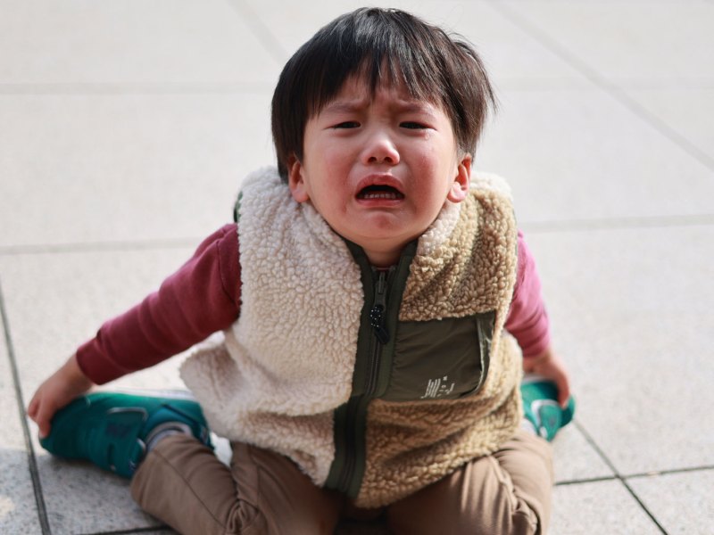 Kleiner Junge, ca. 3 Jahre, sitzt auf dem Steinboden und weint.