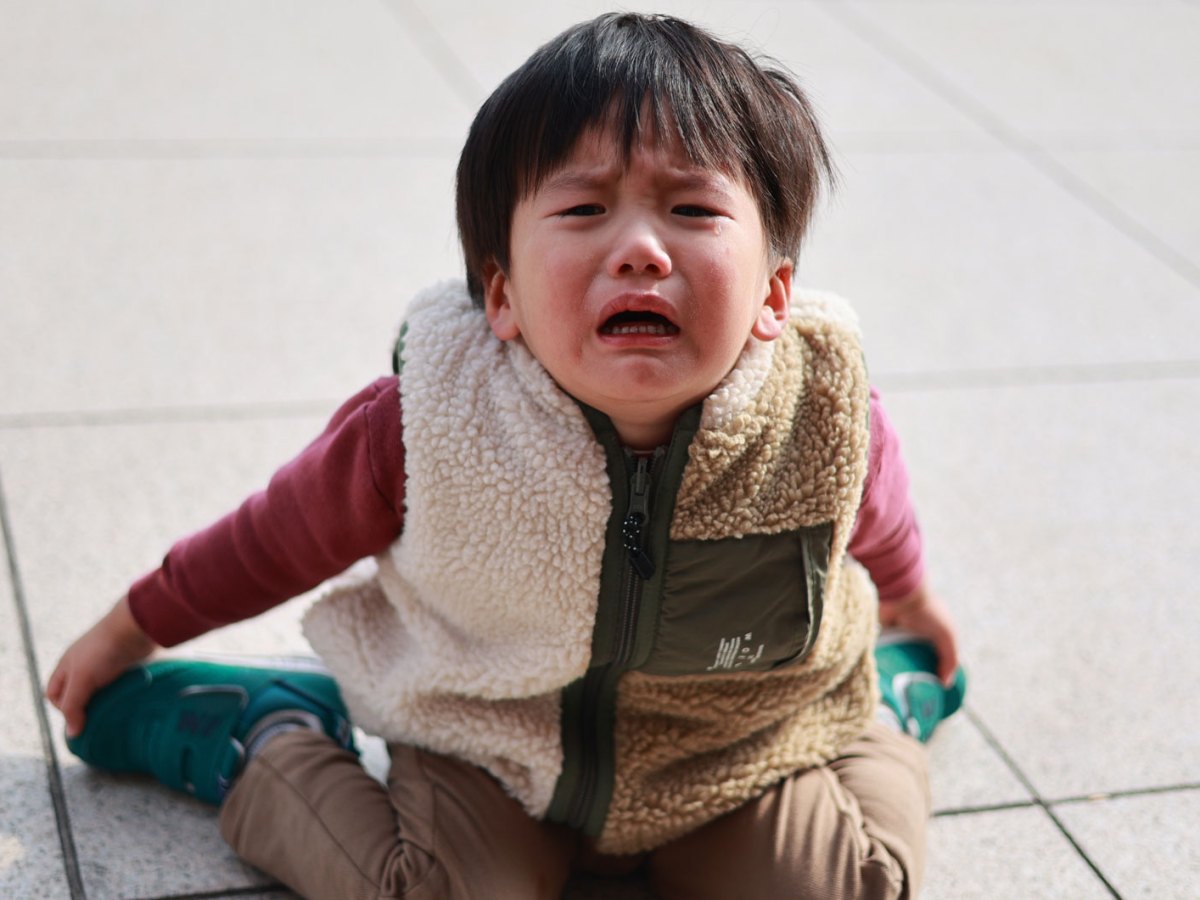 Kleiner Junge, ca. 3 Jahre, sitzt auf dem Steinboden und weint.