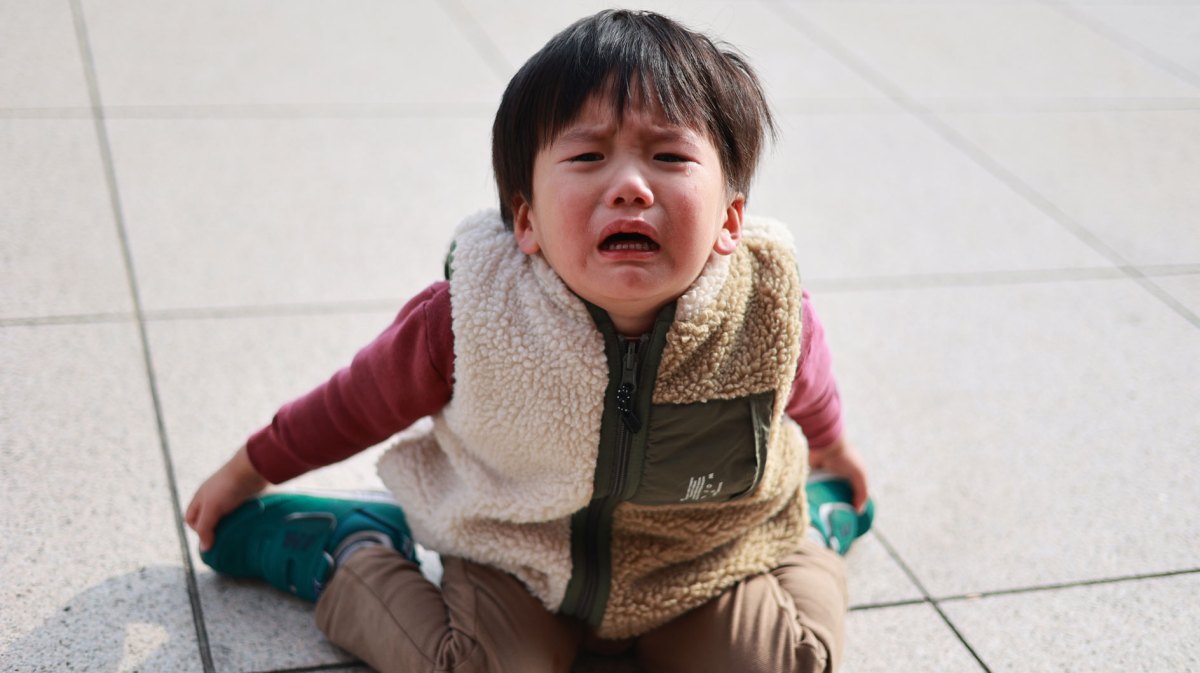 Kleiner Junge, ca. 3 Jahre, sitzt auf dem Steinboden und weint.