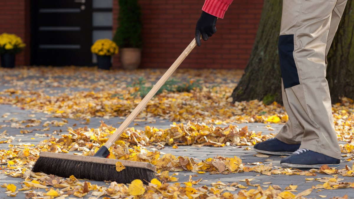 Person fegt Laub vor der Haustüre