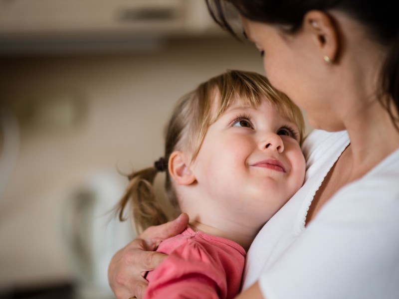 Tochter, ca. 5 Jahre alt, liegt in den Armen ihrer Mama und schaut sie ganz verliebt und glücklich an.