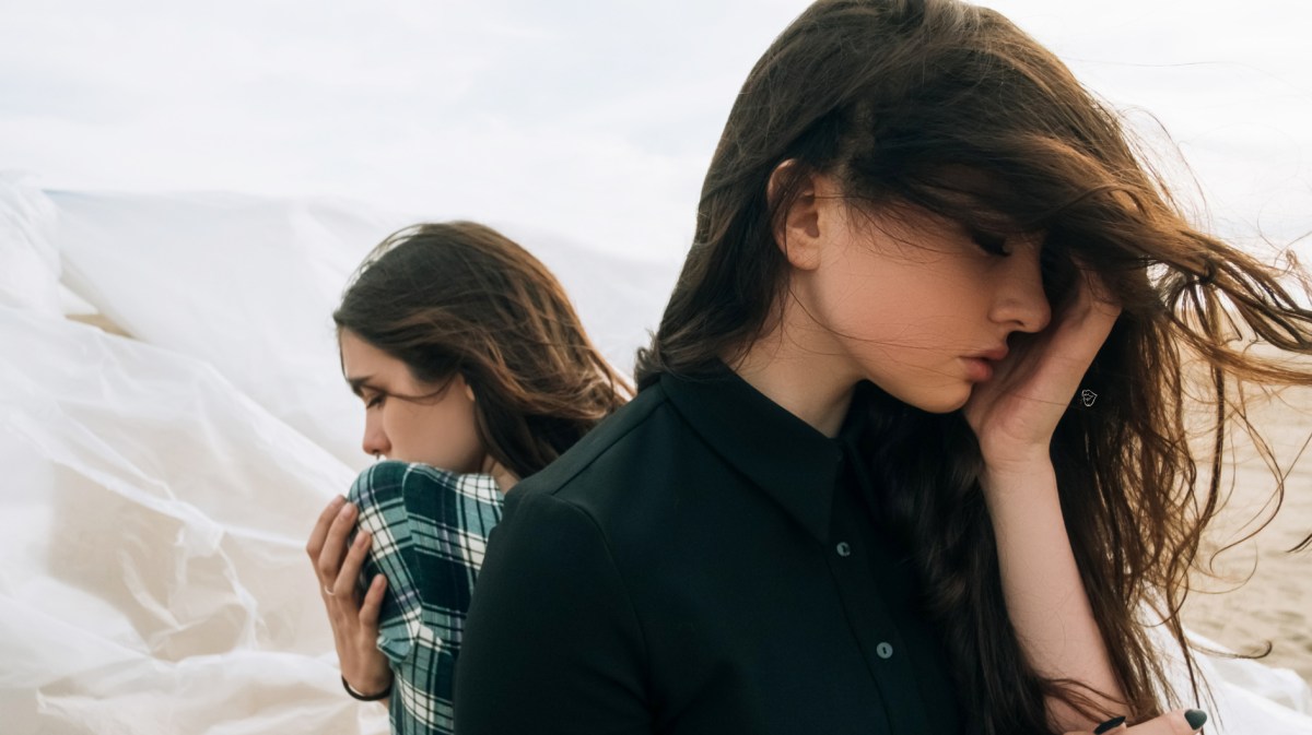 Zwei Frauen, die im Wind draußen stehen und traurig in die jeweils andere Richtung schauen