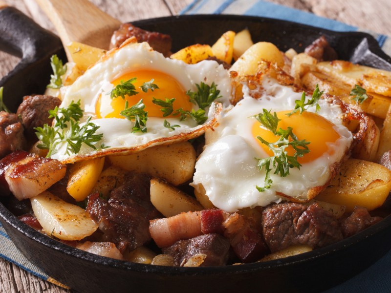 Bauernschmaus mit Kartoffeln, Wurst und Spiegeleier in einer Pfanne.