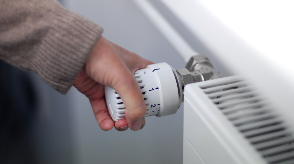 Person dreht an Heizung