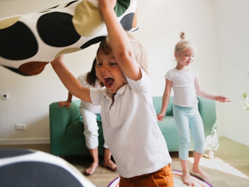 Kinder spielen Wild im Wohnzimmer und werden Kissen.