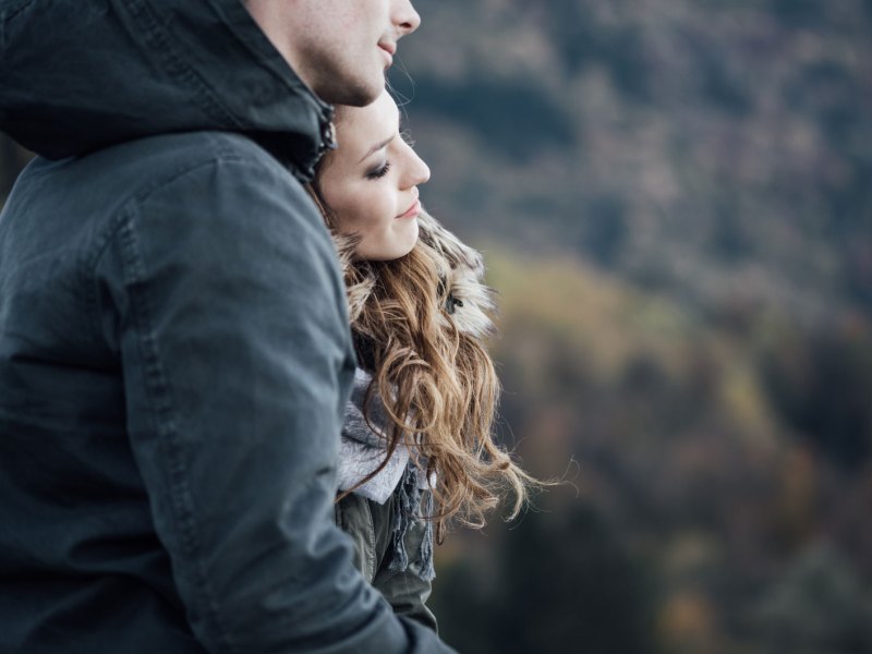 Mann und Frau stehen Arm in Arm auf einem Berg.