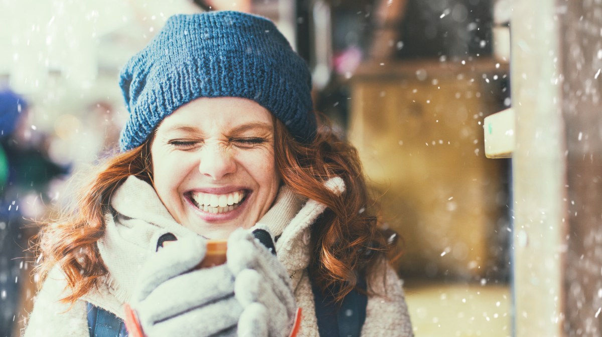 Rothaarige Frau mit einer Tasse in der Hand im Schnee.