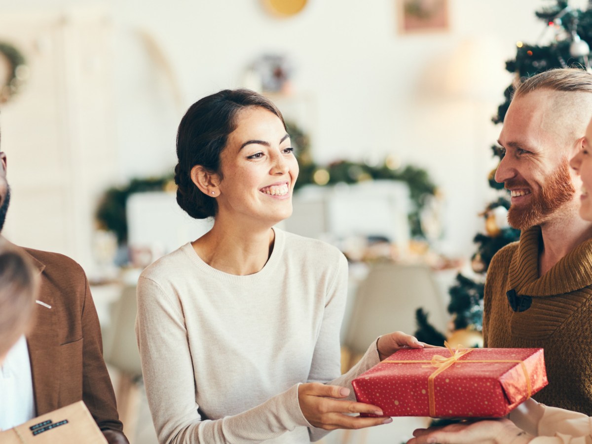 Gruppe von Frauen und Männern überreicht sich gegenseitig Wichtelgeschenke und hat Spaß.