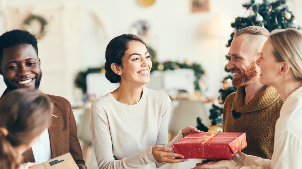 Gruppe von Frauen und Männern überreicht sich gegenseitig Wichtelgeschenke und hat Spaß.