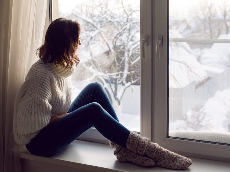 Frau sitzt vor Fenster, dahinter Winterlandschaft