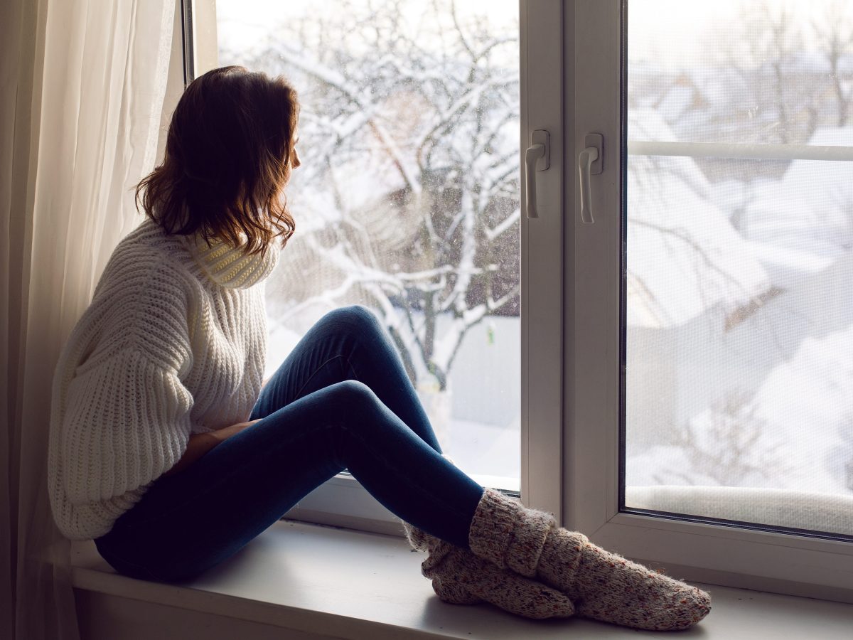 Frau sitzt vor Fenster, dahinter Winterlandschaft