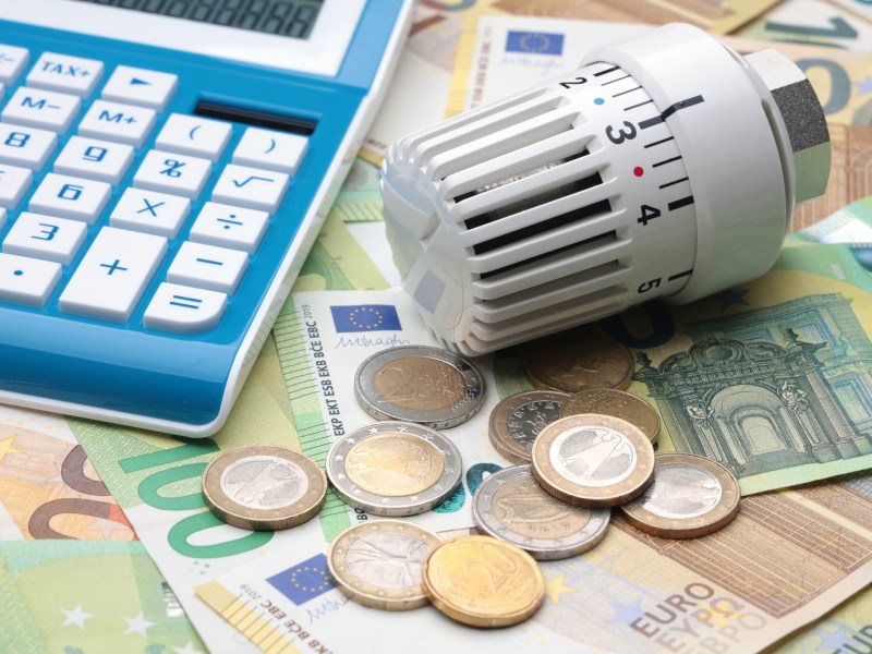 Geldscheine, Münzen, Taschenrechner und Heizungsthermostat auf Tisch