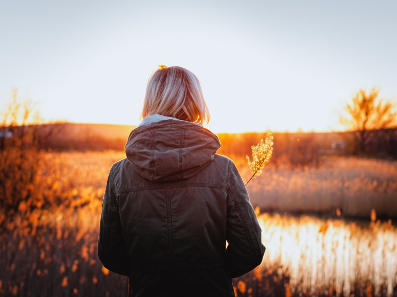 Frau die im Wald steht vor einem See während des Sonnenuntergangs