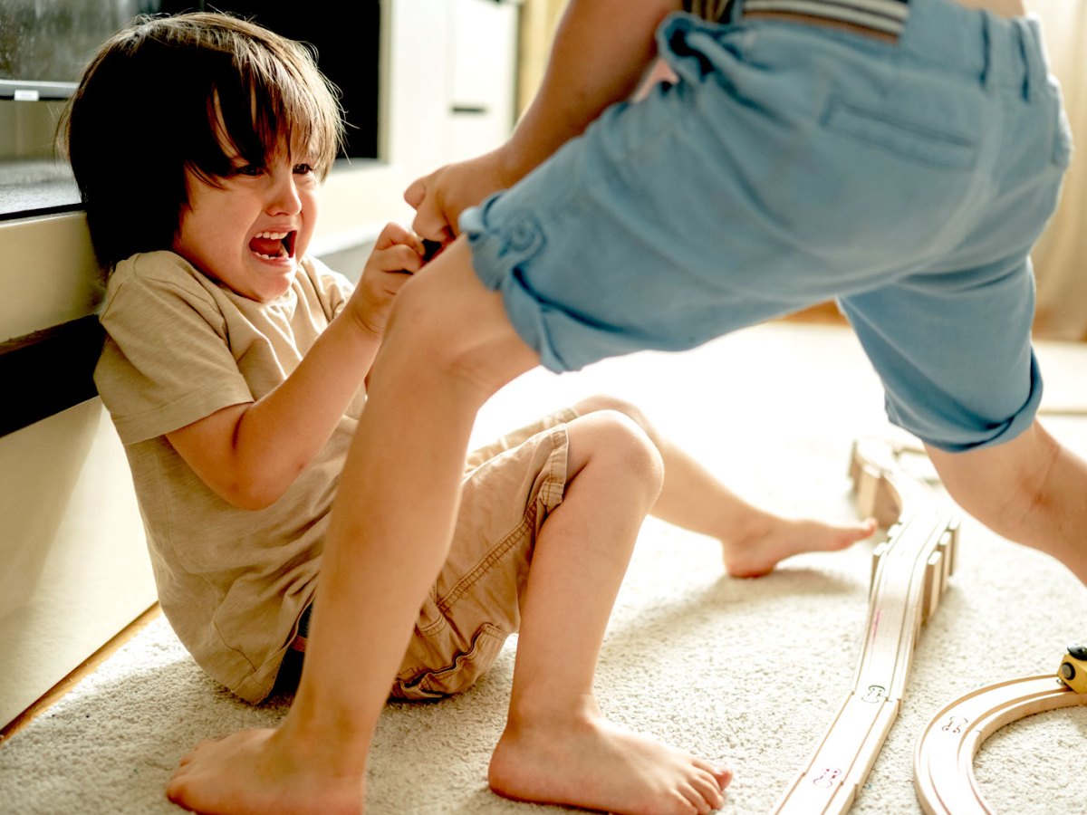 Zwei Jungs streiten sich um ein Spielzeug. Einer sitzt auf dem Boden, der andere steht vor ihm und zieht am Gegenstand.