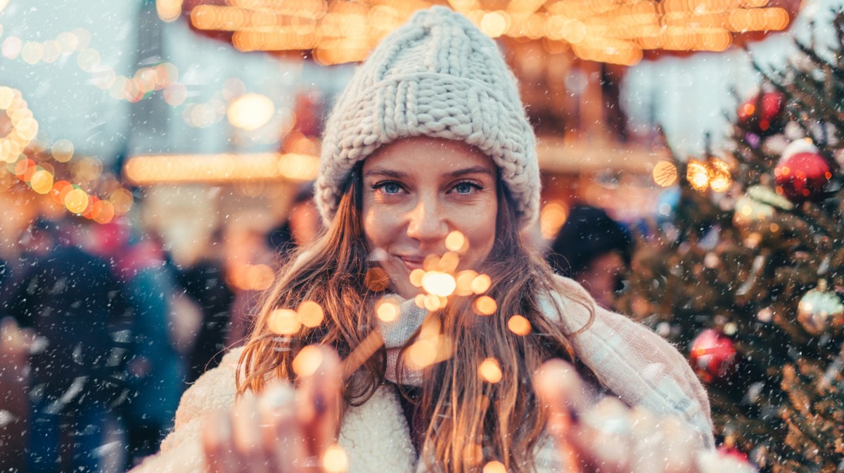 Frau mit Mütze auf dem Weihnachtsmarkt mit Wunderkerze in der Hand