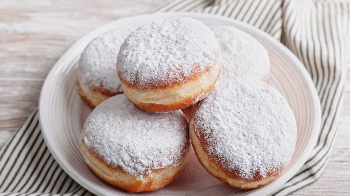 Berliner mit Puderzucker auf einem weißen Teller.