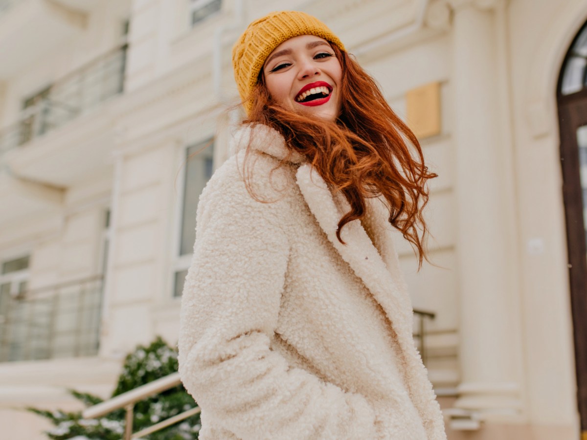 Frau mit roten Haaren trägt weißen Wintermantel.