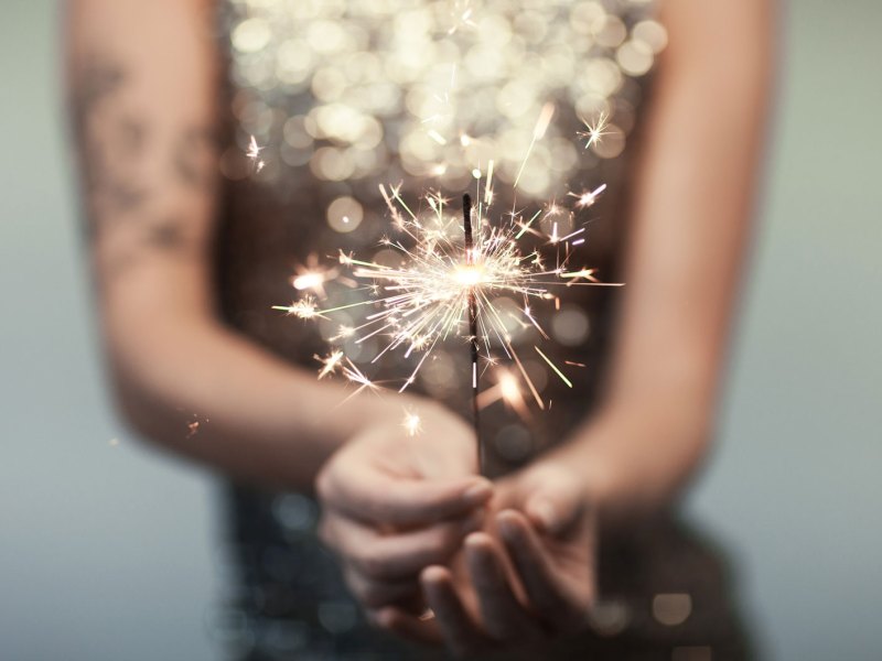 Frau in einem Glitzerkleid hält eine Wunderkerze in der Hand