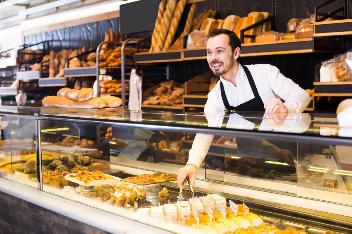 Bäckereiverkäufer hinter seiner Auslage in einem großen Backladen.