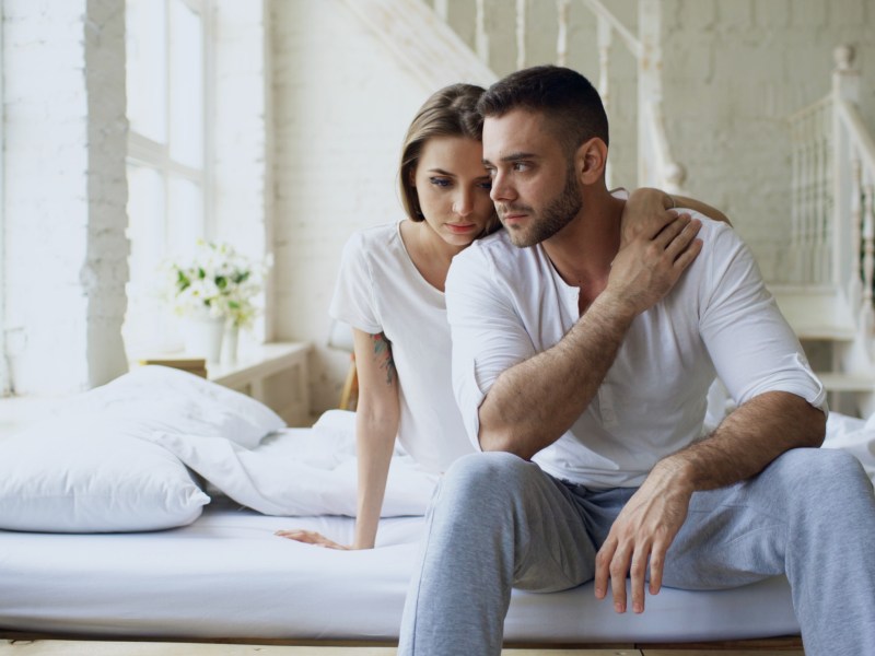 Frau und Mann auf dem Bett, die nachdenklich zur Seite schauen