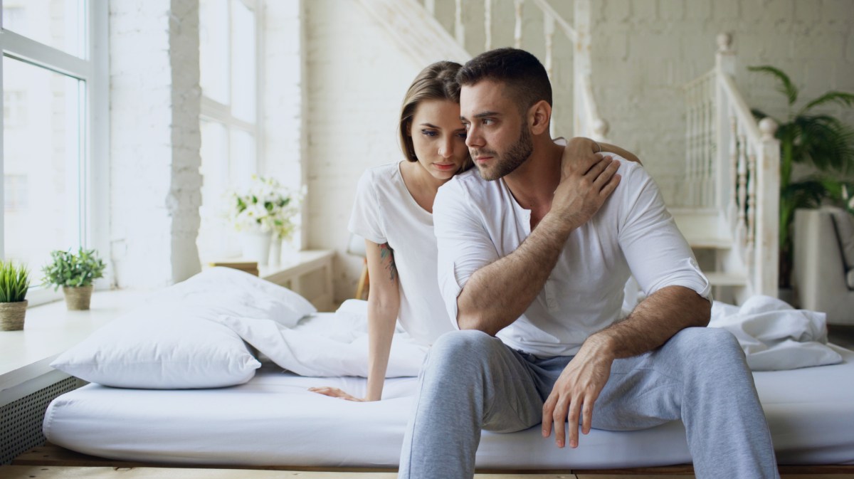 Frau und Mann auf dem Bett, die nachdenklich zur Seite schauen