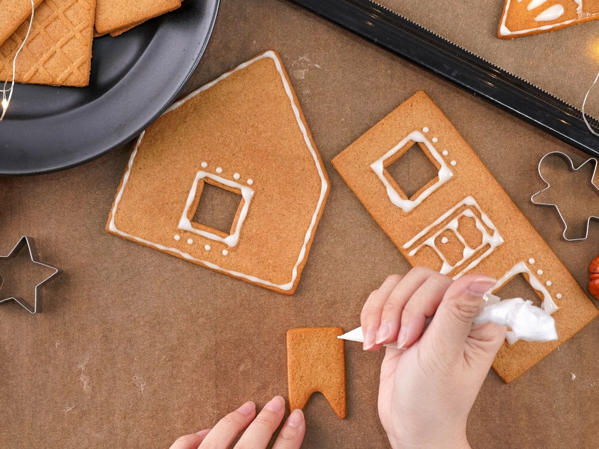 Eine Hand dekoriert Lebkuchen f&uuml;r ein Lebkuchenhaus.