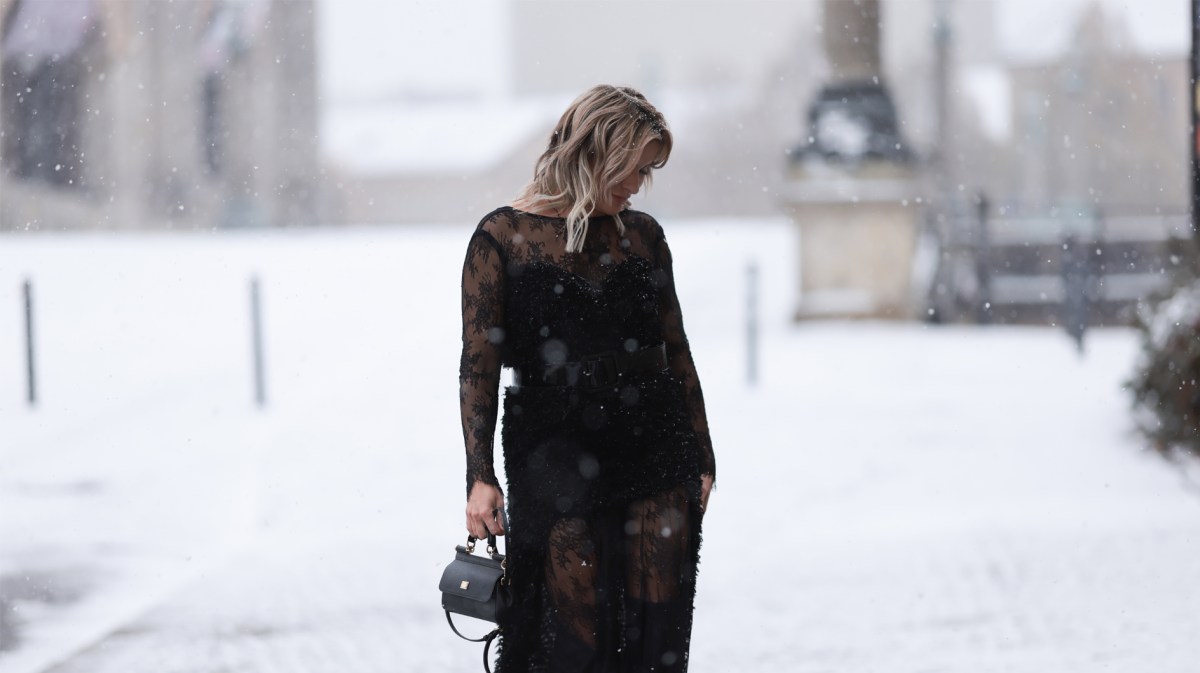 Frau mit schwarzem Kleid beim Winterspaziergang durch den Schnee.