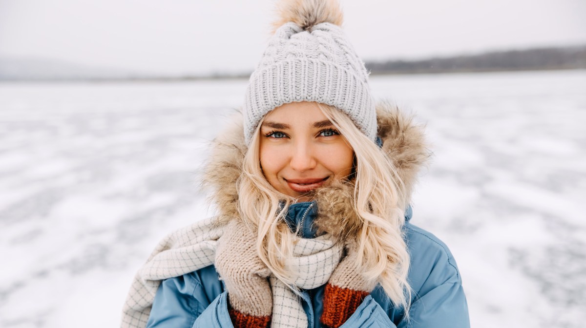 Frau mit blonden Haaren und Mütze im Schnee.