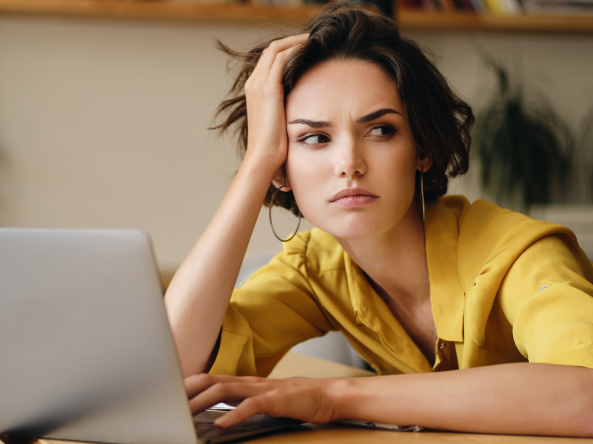 Frau vor einem Computer, die ihre Kopf mit der Hand abst&uuml;tzt und genervt zur Seite blickt.