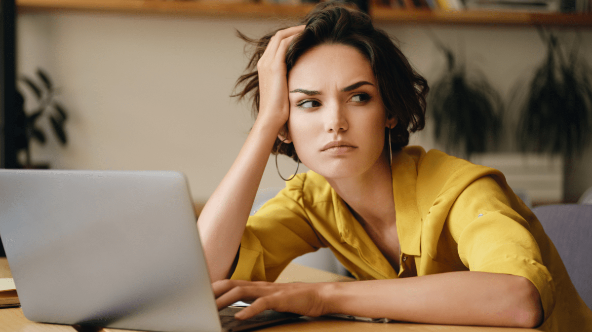 Frau vor einem Computer, die ihre Kopf mit der Hand abstützt und genervt zur Seite blickt.