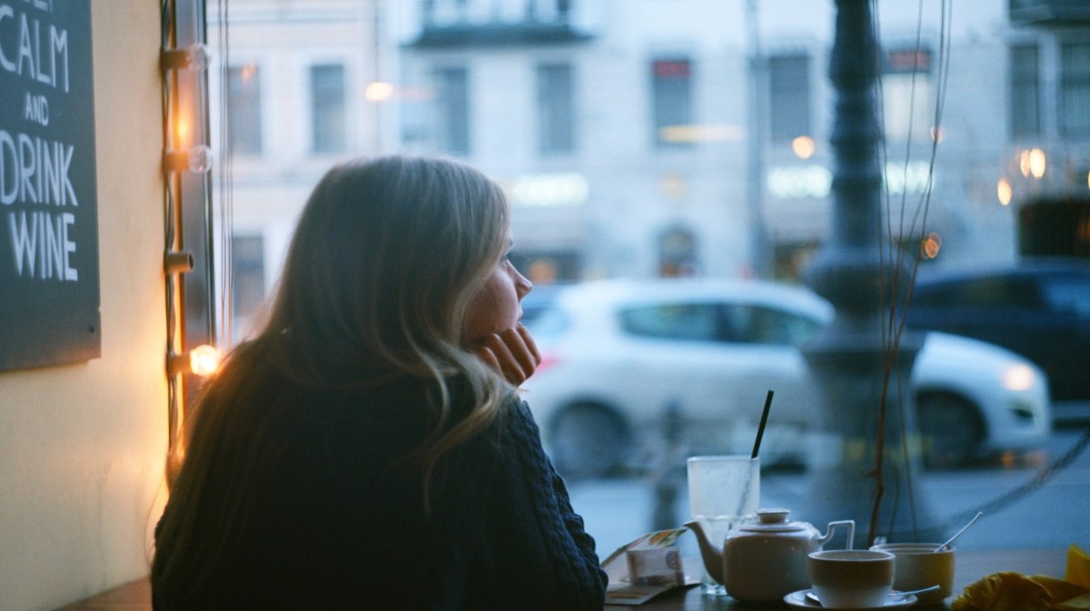 Frau in einem Café am Fenster, die nachdenklich hinausschaut