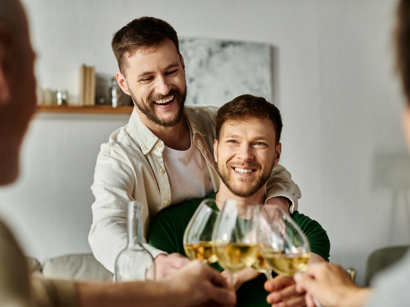 Zwei Männer, die mit einem Weinglas mit zwei anderen Menschen anstoßen.